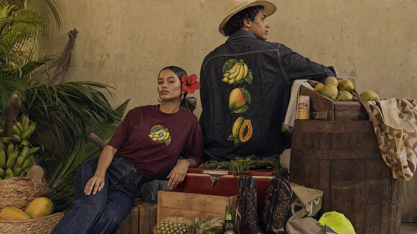 Dos figuras contra una pared de cal, entre cajones y fruta